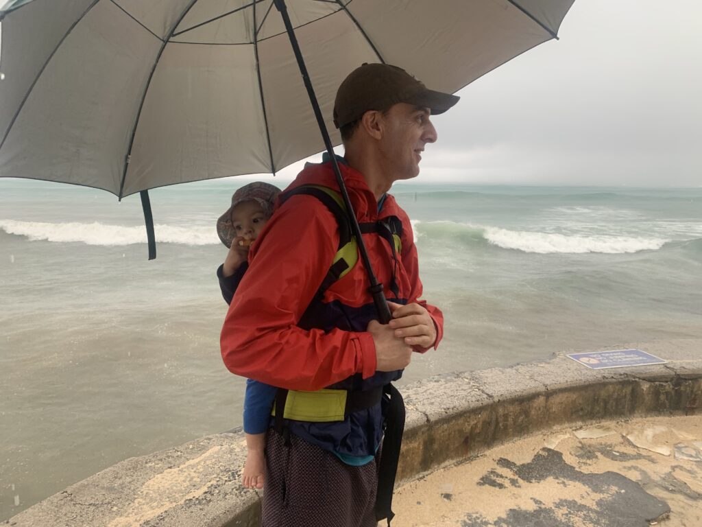 baby in carrier on back of dad under an umbrella